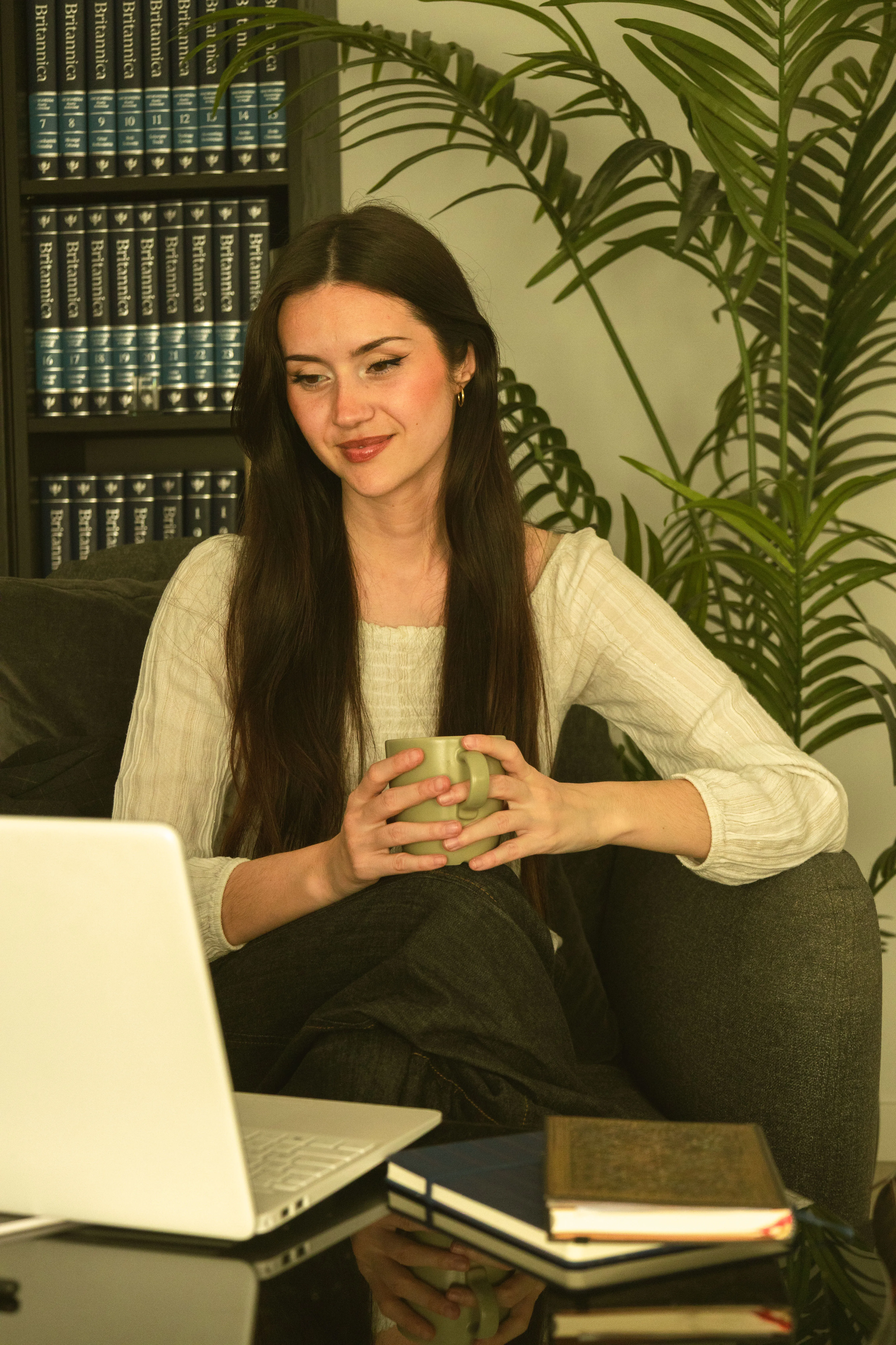 Paula sosteniendo una taza junto a una biblioteca, luz suave de tarde.